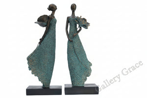 Bronze sculpture of two figures in flowing dresses on a white background