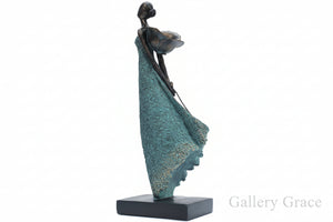 Statue of a woman draped in blue fabric on a wooden surface with a stone wall background